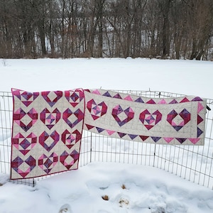 Può includere: Due arazzi a forma di cuore trapuntati in tessuto rosa e bianco. L'arazzo più grande è un runner con un bordo a festoni. L'arazzo più piccolo è quadrato.