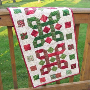May include: A white table runner with a red and green geometric pattern. The pattern is made up of squares and rectangles, and it is reminiscent of a festive design.