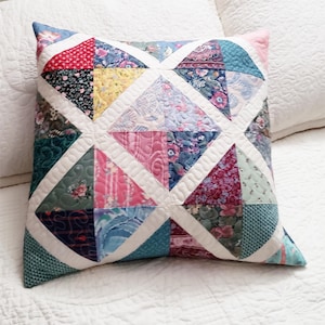 Op de afbeelding: Een patchwork kussen met een ruitpatroon in tinten roze, blauw, groen en wit. Het kussen is gemaakt van verschillende stoffen met bloemen- en geometrische prints.