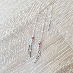 Könnte beinhalten: Ein Paar silberne Ohrringe mit einem silbernen Engelsflügel-Anhänger, rosa und blauen Perlen und einer silbernen Kette.