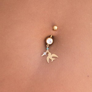 May include: A gold belly button ring with a clear gem and a small bird charm.