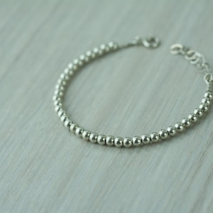 Puede incluir: Un brazalete de plata con cuentas redondas y espaciadas uniformemente. El brazalete tiene un cierre de broche.