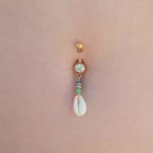 May include: Gold belly button ring with a clear crystal charm and a white seashell dangle.