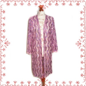 May include: A long, open-front, light purple sequined cardigan with a wavy pattern. The cardigan is displayed on a mannequin. The sleeves and edges are trimmed with a lighter pink fabric. The garment is a formal wear item.