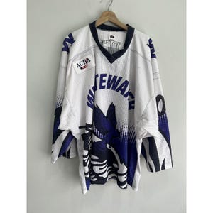May include: White hockey jersey with blue and black accents. The jersey has the text "Whitewater" on the front and a small patch with the text "ACHA" on the left chest.