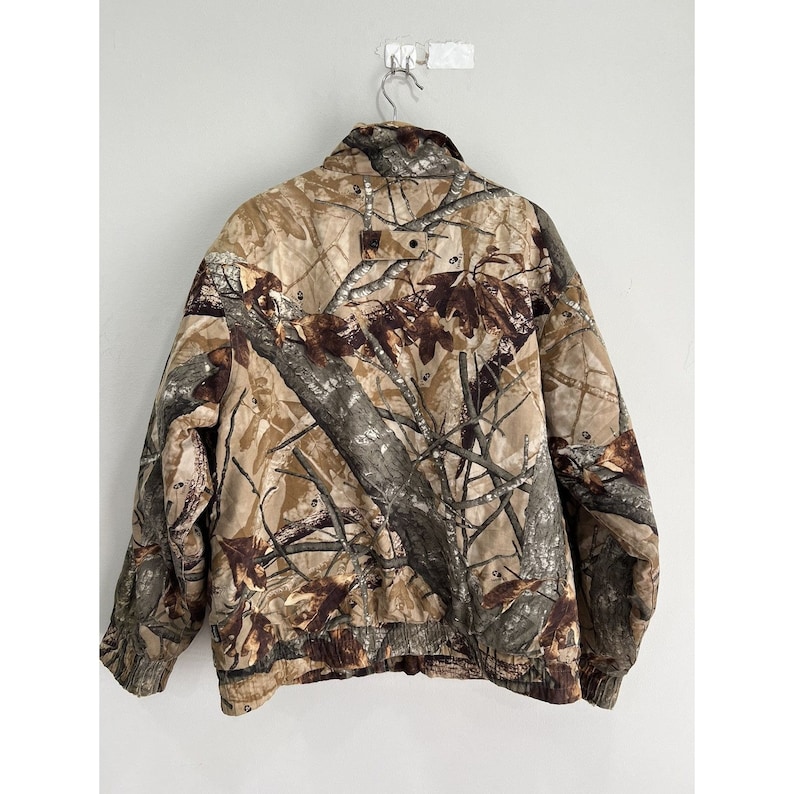 May include: A brown, green, and tan camouflage jacket with a zipper closure. The jacket has a stand-up collar and long sleeves.