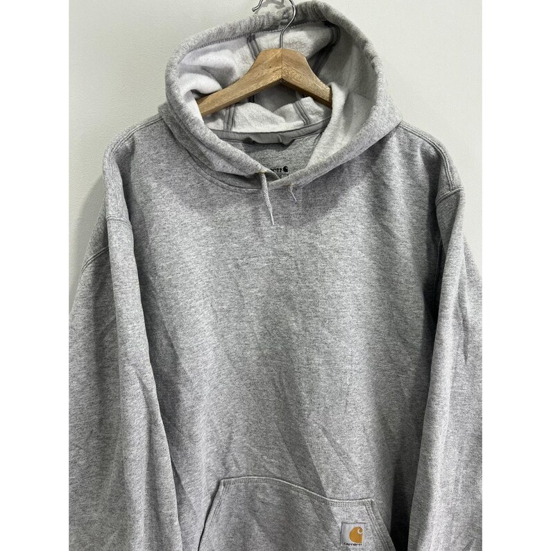 May include: A grey hooded sweatshirt with a small yellow Carhartt logo on the front pocket.