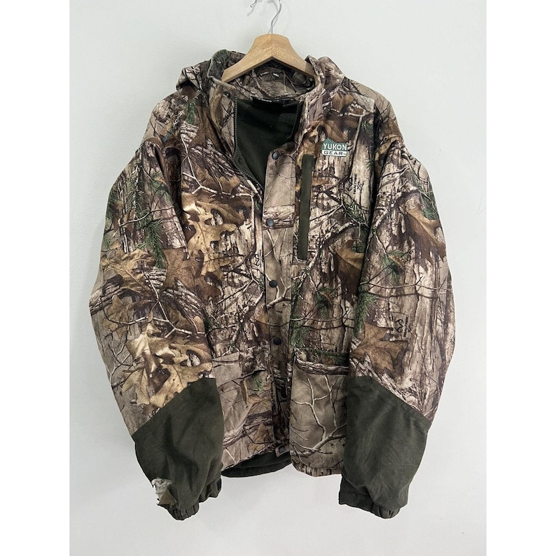 May include: Camouflage jacket with a green logo that says "Yukon Gear". The jacket has a hood and a zipper closure.