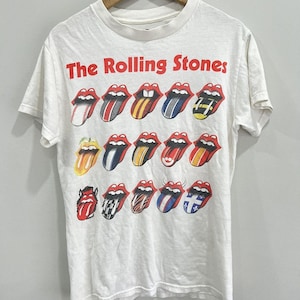 May include: A white short-sleeve t-shirt featuring the red text The Rolling Stones at the top. Below the text are fifteen graphic illustrations of the iconic tongue and lips logo, each filled with a different pattern, color, or design motif.