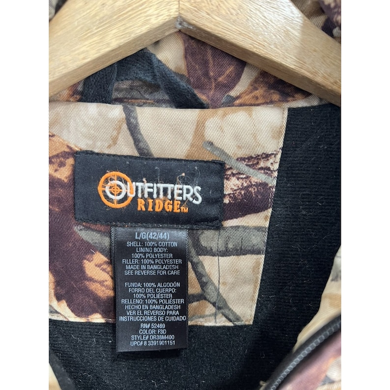 May include: A black and brown camouflage jacket with a black label that reads "Outfitters Ridge" and includes size and care instructions.