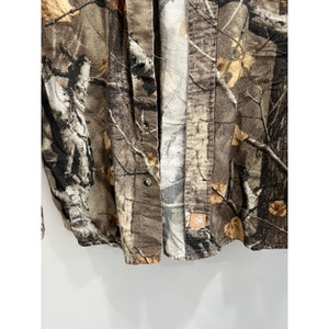 Pu&ograve; includere: Una camicia a maniche lunghe con bottoni di colore mimetico marrone e beige con una piccola toppa marrone in basso a destra.