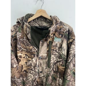 May include: A camouflage-patterned jacket with a hood and a zipper closure. The jacket has a green patch with the text "YUKON GEAR" on the right chest.