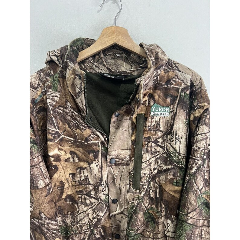 May include: A camouflage-patterned jacket with a hood and a zipper closure. The jacket has a green patch with the text "YUKON GEAR" on the right chest.