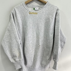 May include: A vintage grey sweatshirt with a crew neck and long sleeves, hanging on a wooden hanger. The sweatshirt has several small holes and a distressed appearance, suggesting it is well-worn. The cuffs and hem are slightly frayed.