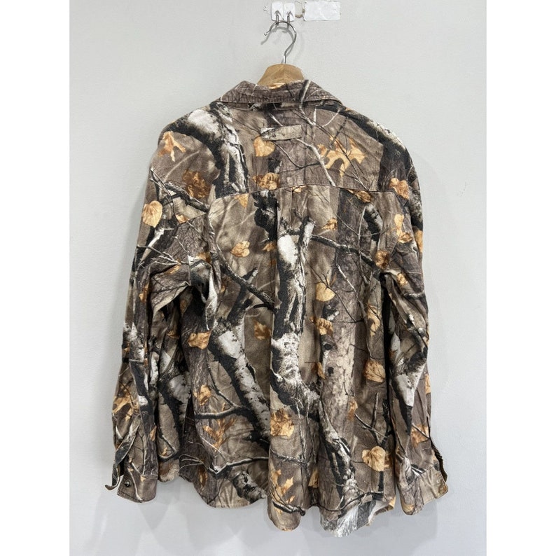 Pu&ograve; includere: Una camicia a maniche lunghe con bottoni e un motivo mimetico marrone e beige. La camicia ha un colletto e una chiusura con bottoni.