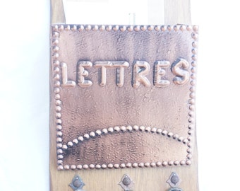 Può includere: Una cassetta delle lettere da parete in legno con un frontale in metallo color rame che dice "LETTRES" in lettere in rilievo. La cassetta delle lettere ha tre ganci per chiavi con chiavi antiche appese.