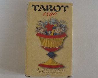 May include: A rectangular tarot card box with the word "TAROT" above "1860" in red. The box features a floral design in a decorative vase with red, yellow, and blue accents. The text "J. GAUDAIS 20 Rue de la Banque. PARIS" is printed at the bottom.