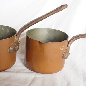 May include: Two copper sauce pans with long handles. The pans are different sizes and have a shiny, metallic finish.