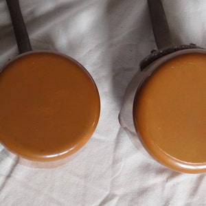May include: Two brown enamel saucepans with black handles. The saucepans are different sizes.