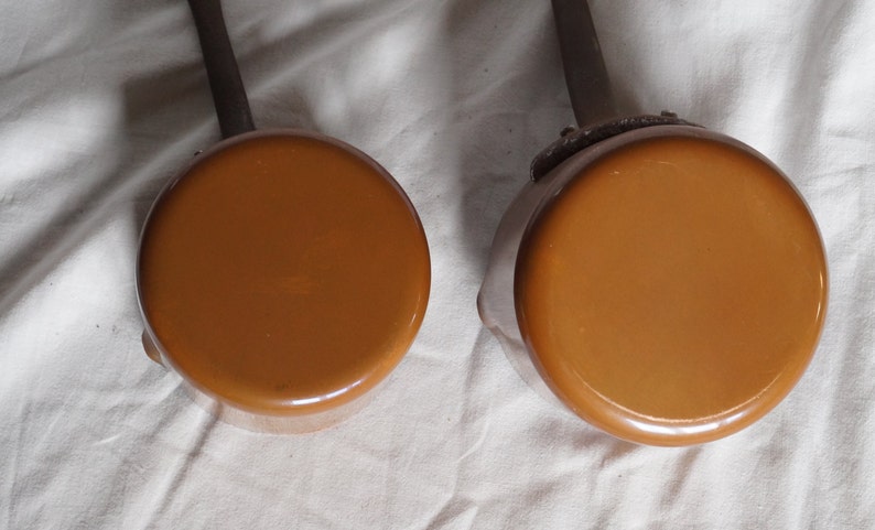 May include: Two brown enamel saucepans with black handles. The saucepans are different sizes.