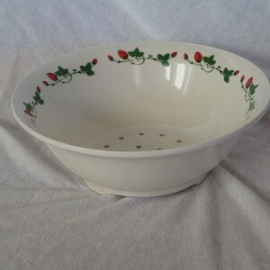 Pode incluir: Escorredor de cerâmica creme com um padrão de morangos e videiras na borda. A tigela tem orifícios de drenagem e uma base. Um artigo de cozinha clássico para lavar frutas e vegetais.