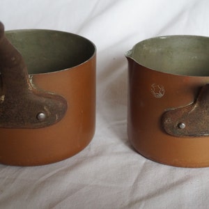 May include: Two small copper pots with iron handles. The pots have a brown patina and are slightly worn.