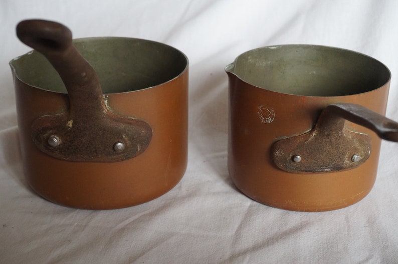 May include: Two small copper pots with iron handles. The pots have a brown patina and are slightly worn.