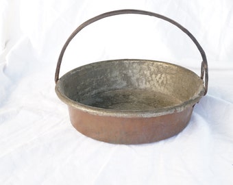 May include: A vintage copper basin with a worn handle. The basin is round and has a slightly tarnished finish.
