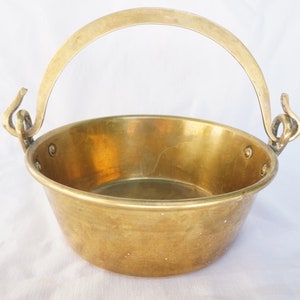 May include: A small, round brass pot with a handle. The pot has a smooth, shiny surface and is ideal for a variety of uses.