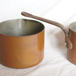 May include: Two copper saucepans with long handles. The saucepans are a warm copper color and have a shiny finish.