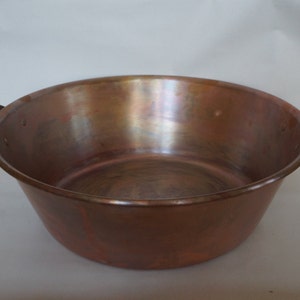 Puede incluir: Una olla grande de cobre con dos asas. La olla está vacía y tiene una superficie brillante y reflectante.