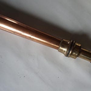 May include: A copper and brass pipe with a threaded end. The pipe is about 18 inches long and has a diameter of about 1 inch.