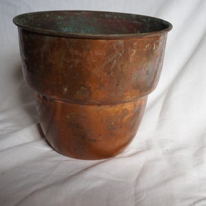 May include: A copper planter with a slightly flared top and a rounded bottom. The planter has a patina finish and appears to be vintage.