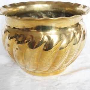 Könnte beinhalten: Ein goldfarbener Messingtopf mit geriffeltem Design. Der Topf hat einen gewellten Rand.