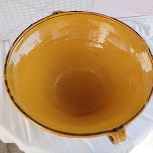 以下が含まれることがあります： テクスチャ加工された内側の大きな丸い黄色のセラミックボウル。ボウルは濃い茶色の縁と片側に小さなハンドルが付いています。ボウルは白い表面にあります。