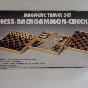 Könnte beinhalten: Eine Holzkiste mit einem magnetischen Reisespiel mit Schach, Backgammon und Dame. Die Kiste ist in Braun und Schwarz gehalten und auf der Vorderseite steht "MAGNETIC TRAVEL SET CHESS-BACKGAMMON-CHECKERS". Auf der Vorderseite der Kiste steht auch "3 in 1 Games".