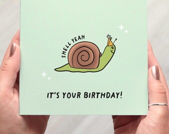 May include: A light green birthday card featuring a cartoon snail with a party hat. The snail has a brown shell and is smiling. Text on the card reads "SHELL YEAH" and "IT'S YOUR BIRTHDAY!" with sparkling star accents.
