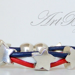 May include: A red, white, and blue leather bracelet with silver star charms. The bracelet is woven with three strands of leather.