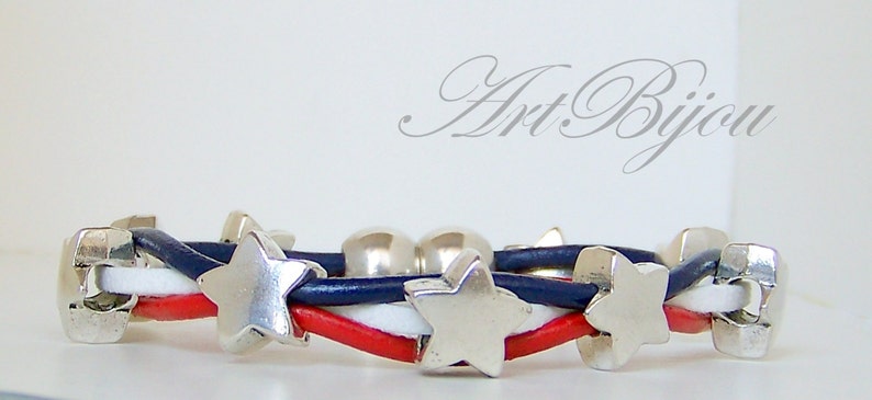 May include: A red, white, and blue leather bracelet with silver star charms. The bracelet is woven with three strands of leather.