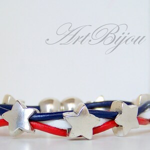 May include: A red, white, and blue leather bracelet with silver star charms. The bracelet is woven with three strands of leather, each a different color. The stars are evenly spaced along the bracelet.