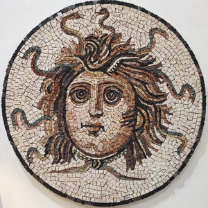 May include: A round mosaic artwork depicting Medusa, a Greek mythological figure with snakes for hair. The mosaic is made of small, colorful tiles and features a detailed depiction of Medusa's face and snakes.