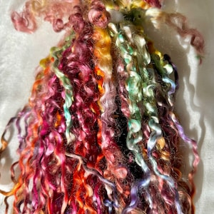 May include: A bundle of colorful, curly yarn in shades of pink, orange, green, and purple. The yarn is arranged in a loose, flowing pile.