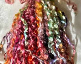 May include: A bundle of colorful, curly yarn in shades of pink, orange, green, and purple. The yarn is arranged in a loose, flowing pile.