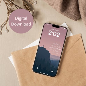 以下が含まれることがあります： スマートフォンには、山のシルエットと「Not all those who wander are lost」という引用句が表示されたデジタル壁紙が表示されています。画面には、6月14日金曜日の2時02分が表示されています。「Digital Download」というピンク色の円が左上にあります。