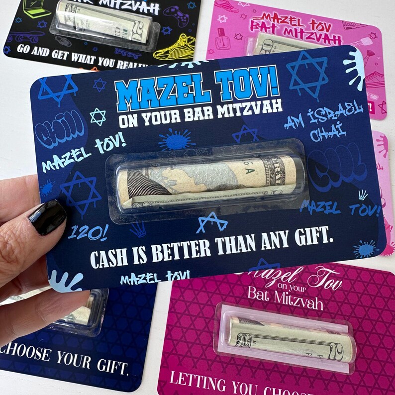 May include: A blue and white card with a Star of David design and the text "Mazel Tov! On Your Bar Mitzvah" and "Cash is better than any gift." A rolled up banknote is visible in a clear plastic pocket on the card.
