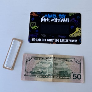 May include: A black card with a colourful design featuring a skateboard, a laptop, and a video game controller. The text "Mazel Tov Bar Mitzvah" is written in a graffiti style font. The card also includes the text "Go and get what you really want!" and a blank space for a gift card amount.