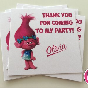 May include: Thank you for coming to my party!  A pink Trolls character with blue eyes and a flower crown is on a white thank you card with the name Olivia.