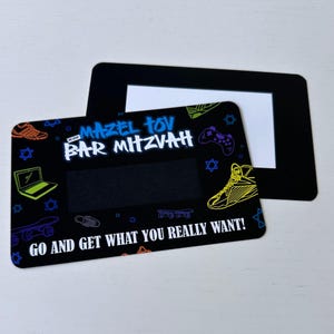 May include: Black and white card with a colourful design featuring a laptop, trainers, skateboards, and a video game controller. The text "Mazel Tov Bar Mitzvah" is in blue and white. The text "Go and get what you really want!" is in white.