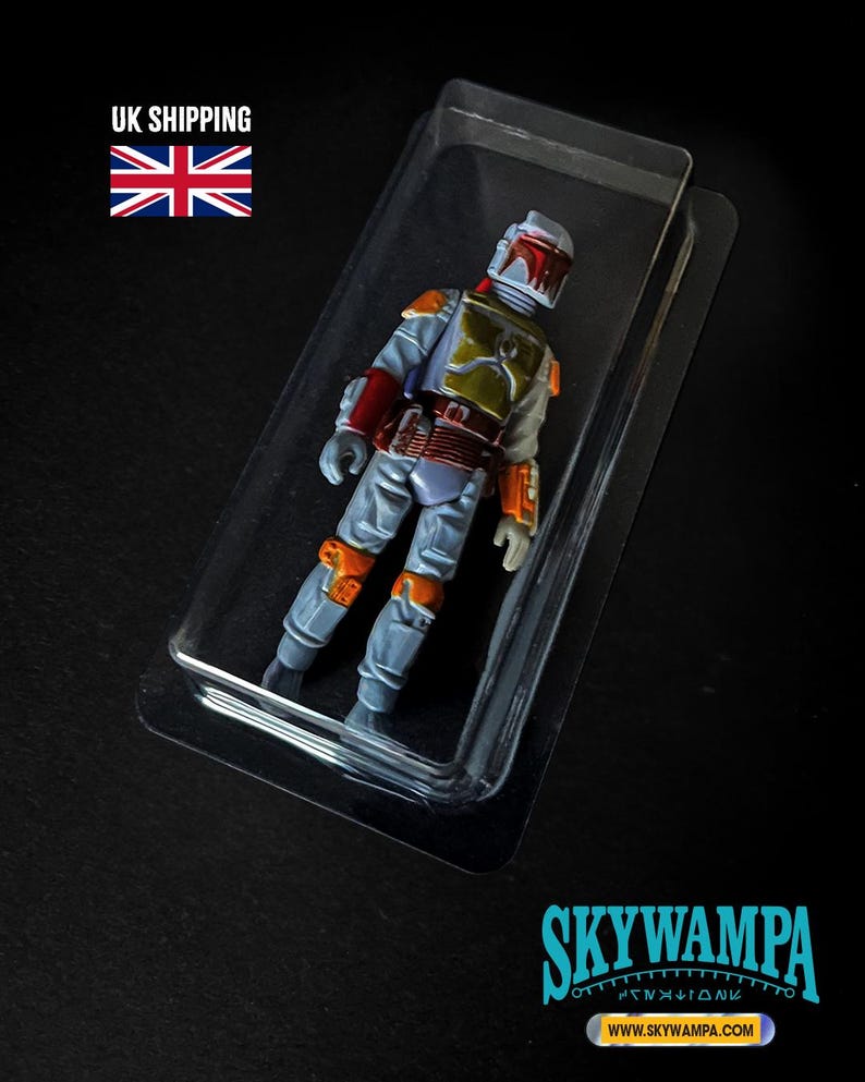 May include: A Boba Fett action figure encased in a clear plastic blister pack. The figure features a light gray jumpsuit, a green chest plate, orange shoulder and knee armor, and a helmet with a red visor. The text SKYWAMPA and WWW.SKYWAMPA.COM appear.