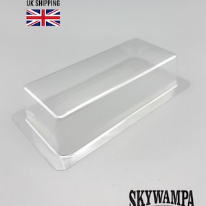 May include: A clear, rectangular plastic blister pack tray with a raised center section and a flat surrounding flange. The tray is transparent and molded into a simple box shape, designed for protective packaging of small items or collectibles.